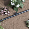 Black irrigation tube on soil with plants and flowers in the background