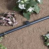 Black irrigation tube on soil with plants and flowers in the background