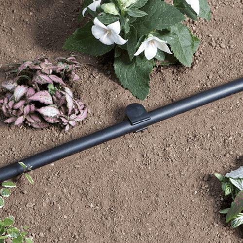 Black irrigation tube on soil with plants and flowers in the background