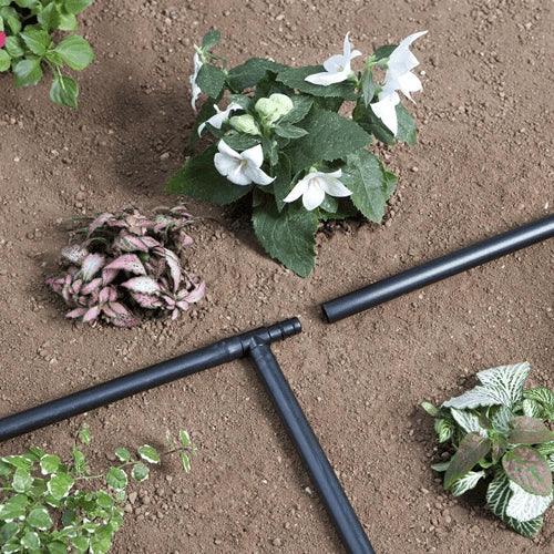 Black garden irrigation system components on a soil background with plants.