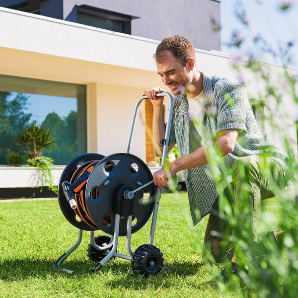Man using a Claber Metal 60 garden hose reel in a backyard setting