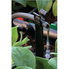 Close-up of a garden irrigation system with water flowing through a nozzle surrounded by green plants.