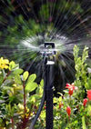 Sprinkler spraying water in a garden with greenery and flowers.