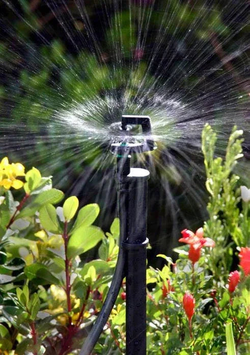 Sprinkler spraying water in a garden with greenery and flowers.