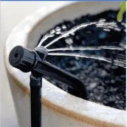 Sprinkler head attached to a hose, spraying water into a pot with soil.