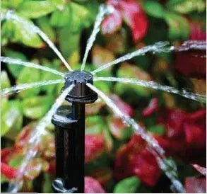 Sprinkler spraying water in a garden with green and red foliage.