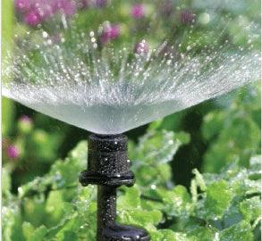 Sprinkler spraying water in a garden with greenery and flowers in the background