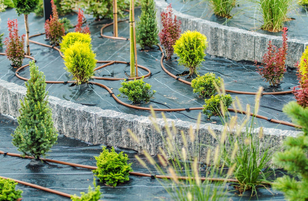 Drip irrigation system with brown hoses watering landscaped garden plants on black weed barrier