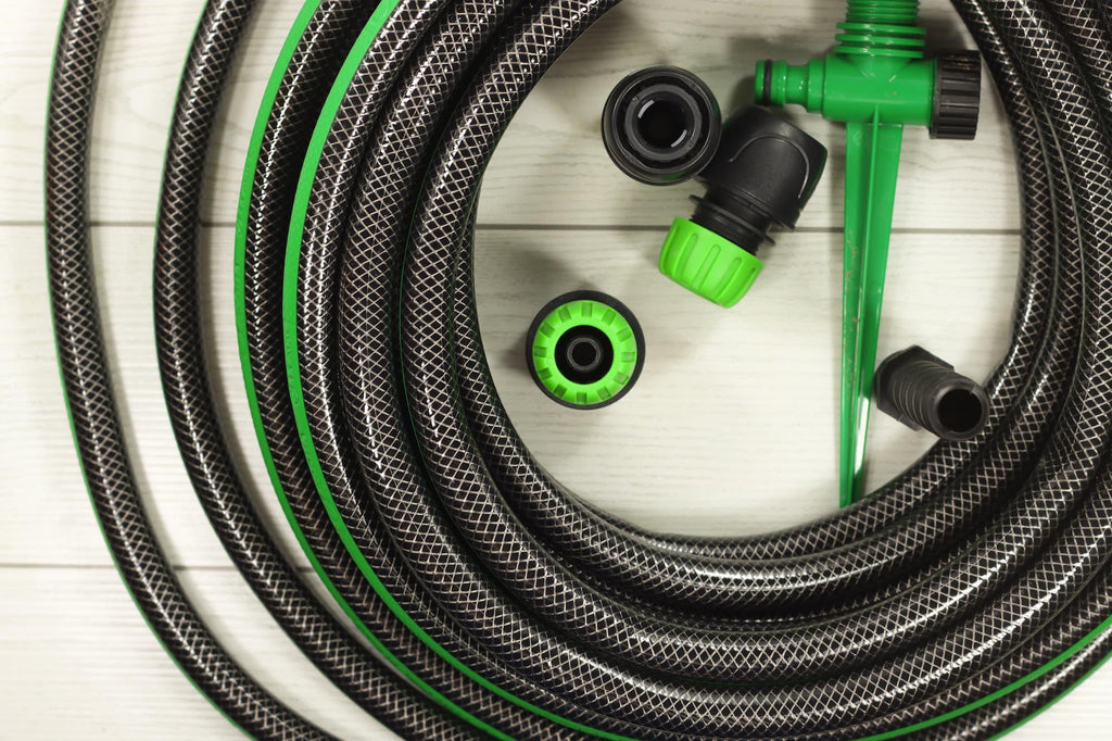 Coiled garden irrigation hose with green connectors and spray nozzle on light wood