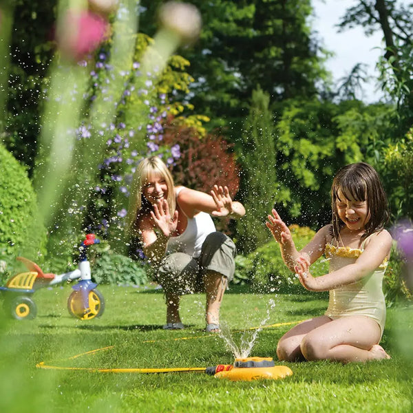 Two children playing with a Hozelock sprinkler in a garden on a sunny day.