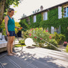 Woman watering plants on a wooden deck with a house and garden in the background